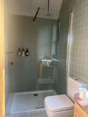 Se trata de un cuarto de baño moderno con azulejos verdes, una zona de ducha, accesorios de baño suspendidos, un inodoro blanco, una mampara de cristal, un lavabo pequeño y luz natural. Diseño minimalista.