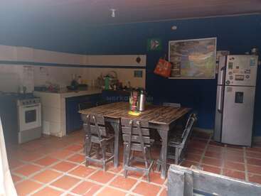 Das Bild zeigt eine rustikale Küche mit dunklen Holzmöbeln, einem zentralen Tisch mit sechs Stühlen, einem Kühlschrank, einem Herd, einer Spüle und blauen Wänden mit Dekorationen.