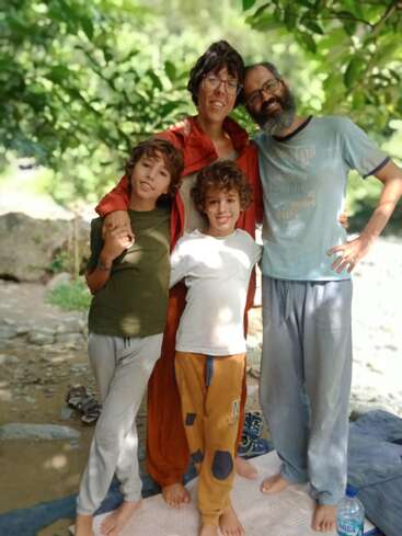 The image depicts a family of four standing together, with two children in front and a man and woman behind them, posing for a photo in a natural outdoor setting.