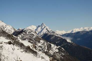 Majestätische, schneebedeckte Berge ragen steil unter einem strahlend blauen Himmel empor. Schroffe Gipfel, tiefe Täler und Waldflecken bilden eine atemberaubende und friedliche Winterlandschaft.