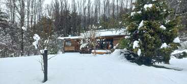 Eine Holzhütte steht eingebettet zwischen schneebedeckten Bäumen in einer ruhigen Winterlandschaft. Eine dicke Schneedecke bedeckt den Boden und schafft eine friedliche, stille und gemütliche Atmosphäre.