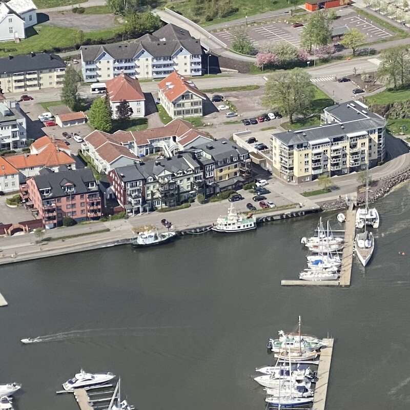 Das Bild zeigt eine ruhige Szene am Wasser mit einer Reihe von Häusern am Ufer und einem Steg und Booten im Hintergrund, die ein Gefühl von Ruhe und Entspannung vermitteln.