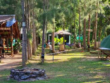 La imagen muestra un entorno sereno al aire libre, con un edificio de madera, hamacas y una tienda de campaña, rodeados de árboles y exuberante vegetación, que desprenden una atmósfera de paz.