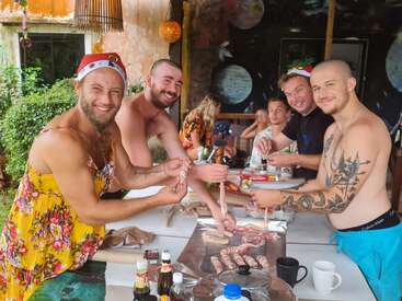 La imagen muestra a cuatro hombres reunidos en torno a una mesa, preparando comida y bebida, con un ambiente festivo que sugiere una celebración festiva, probablemente la Navidad.