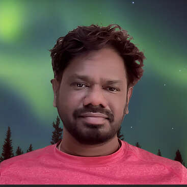 A man with dark hair and a beard wears a pink shirt, standing in front of a scenic background with northern lights and silhouetted pine trees at night.