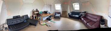 This room features three sofas, two windows, a desk with electronic equipment, cardboard on the floor, a few small tables, and scattered miscellaneous items.