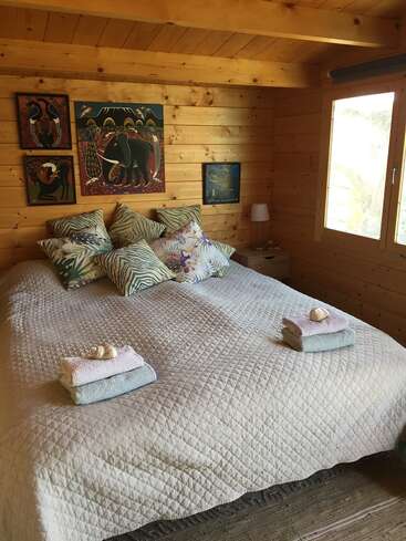 Das Bild zeigt ein gemütliches Schlafzimmer mit einem großen Bett, das mit weißen Decken und farbenfrohen Kissen geschmückt ist und vor einer Wand mit heller Holzverkleidung steht.