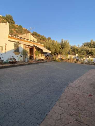 Das Bild zeigt ein ruhiges Haus im spanischen Stil mit einer geräumigen Auffahrt, umgeben von üppigem Grün und einem klaren blauen Himmel, der ein Gefühl von Ruhe und Wärme ausstrahlt.