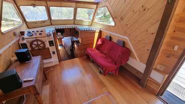 Das gemütliche Boot hat Holzwände und -böden, große Fenster, ein Steuerrad, einen kleinen Tisch mit Lautsprechern, einen rot bezogenen Futon und ein kleines Schlafzimmer.