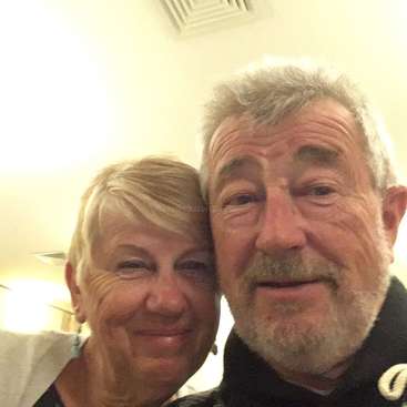 The image shows a selfie of an older man and woman, with the woman on the left and the man on the right, both smiling.