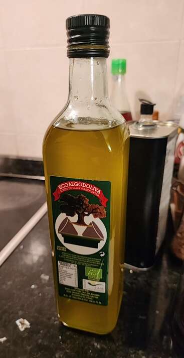 Uma garrafa de azeite de oliva extra virgem EcoalGodOliva está sobre o balcão de uma cozinha. O rótulo verde apresenta uma árvore e contém informações sobre o produto em espanhol.