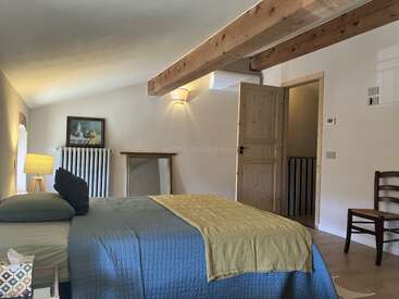 Este quarto aconchegante tem uma grande viga de madeira, uma cama de casal com roupa de cama azul e amarela, móveis de madeira, iluminação suave, um espelho e uma decoração rústica.