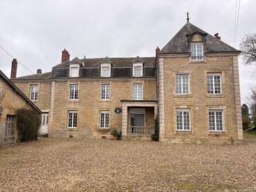 This image shows a large, old stone house with multiple windows, a central entrance, and a gravel courtyard. The sky is overcast and gray.