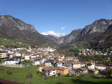 Nestled in a lush valley, a quaint town with colorful houses is surrounded by towering mountains and a backdrop of distant, snow-capped peaks under clear skies.