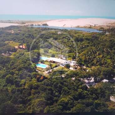 Une vue aérienne époustouflante dévoile un paysage verdoyant, une maison avec piscine, des arbres touffus, une rivière, des dunes de sable et, au loin, l'océan bleu.