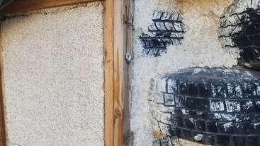 Esta imagen muestra un tramo de pared con estructura de madera, yeso texturizado y neumáticos incrustados y pintados de negro, que podría formar parte de un edificio ecológico o de una instalación de arte reciclado.