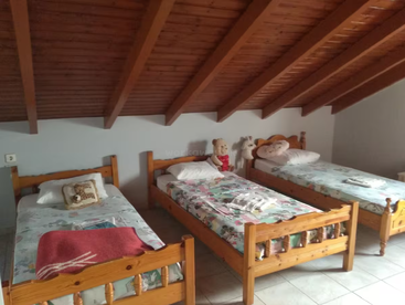 Dieses gemütliche Schlafzimmer im Dachgeschoss verfügt über drei Einzelbetten aus Holz mit geblümter Bettwäsche, eine schräge Holzdecke, Stofftiere auf den Betten und Fliesenböden, die für eine warme Atmosphäre sorgen.