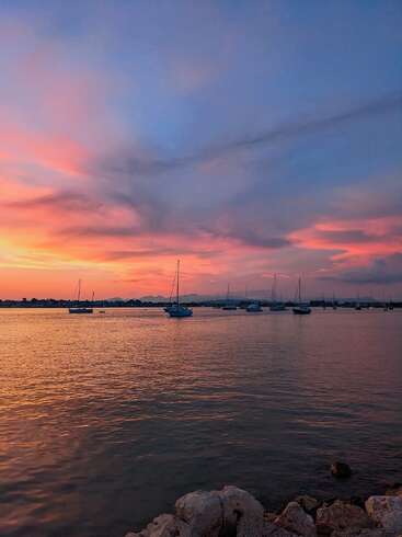 Ein ruhiger Hafen bei Sonnenuntergang, Boote liegen sanft vor Anker. Der Himmel ist in Rosa-, Orange- und Blautöne getaucht, die sich wunderschön im ruhigen Wasser spiegeln.