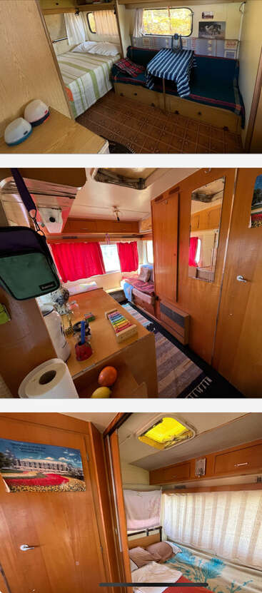 This cozy camper interior features beds, seating areas with tables, warm wooden cabinets, red curtains, small decorations, and natural light, creating a comfortable, homely atmosphere.