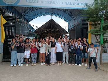 Eine fröhliche Gruppe von Schülern und Lehrern posiert gemeinsam vor der Peace International School, lächelt und macht Friedenszeichen, um die Einheit und Vielfalt in der Bildung zu feiern.