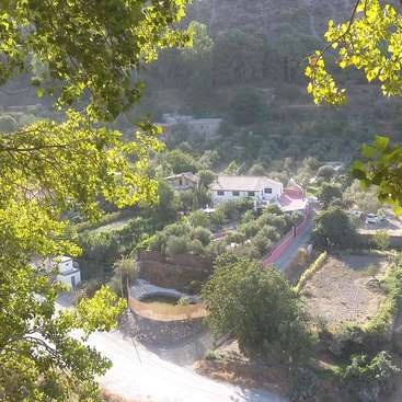 The image depicts a serene rural landscape with a white house, trees, and a road, captured from an elevated perspective, possibly from a hill or mountain.