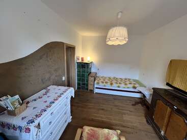 Dieses gemütliche Zimmer verfügt über Holzböden, ein Einzelbett mit gemusterter Bettwäsche, Vintage-Möbel, eine Kommode mit weißem Blumenmuster, eine Hängelampe und eine sanfte, warme Beleuchtung.