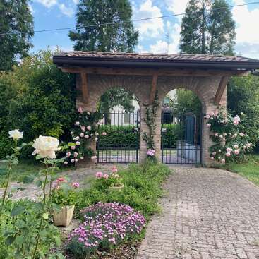 A imagem mostra uma charmosa estrutura de tijolos em arco com um telhado de telhas, cercada por uma vegetação exuberante e flores vibrantes, criando uma atmosfera serena e convidativa.