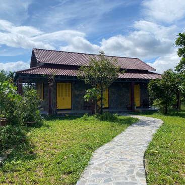 Une charmante maison rustique au toit de tuiles rouges et aux portes jaune vif se trouve au milieu d'une verdure luxuriante. Un sentier en pierre mène à travers le jardin animé.