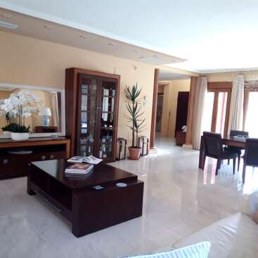 Este espacioso y moderno salón-comedor cuenta con grandes ventanales, muebles de madera oscura, una vitrina, plantas de interior, tonos neutros, iluminación tenue y orquídeas decorativas expuestas.