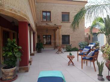 Dieser einladende Innenhof ist mit bequemen blauen Polstersesseln, tropischen Pflanzen, Topfpflanzen, Fliesenboden und warmen Ziegelwänden ausgestattet und bietet einen eleganten, entspannenden Sitzbereich im Freien.