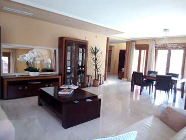 Dieser geräumige, moderne Wohn-Essbereich verfügt über große Fenster, dunkle Holzmöbel, eine Glasvitrine, Zimmerpflanzen, neutrale Töne, sanfte Beleuchtung und dekorative Orchideen.