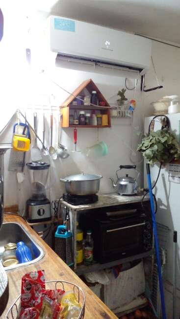 Uma cozinha pequena e aconchegante com utensílios de cozinha, liquidificador, chaleira, ar-condicionado, temperos, forno e lanches. Há uma cesta de batatas fritas sobre a bancada de madeira.