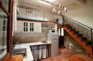 Esse loft aconchegante tem uma cozinha rústica com armários brancos, uma geladeira pequena, detalhes em madeira, paredes de pedra, piso de azulejo e uma escada charmosa que leva ao andar de cima.