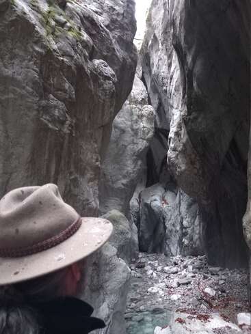 Das Bild zeigt einen Mann mit Hut, der in einer engen Schlucht steht, durch die ein Bach fließt, mit großen Felsen auf beiden Seiten.