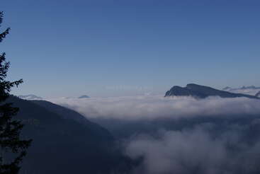 Eine atemberaubende Berglandschaft mit dunklen Bergkämmen erhebt sich über einem weißen Wolkenmeer unter einem klaren blauen Himmel, der Ruhe und natürliche Erhabenheit ausstrahlt.