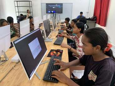 A group of students sits at computers in a classroom, focused on their screens, learning and working together in a modern educational environment with technology.