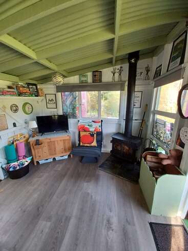 Cette pièce chaleureuse est équipée d'un poêle à bois, d'une décoration colorée, de livres, d'une télévision, d'œuvres d'art ludiques, de sièges confortables, d'un parquet et de grandes fenêtres laissant entrer la lumière naturelle.