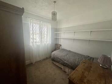 Il s'agit d'une petite chambre confortable avec un lit simple, des meubles en bois, des étagères, une fenêtre avec des rideaux blancs, des murs et une moquette de couleur neutre.
