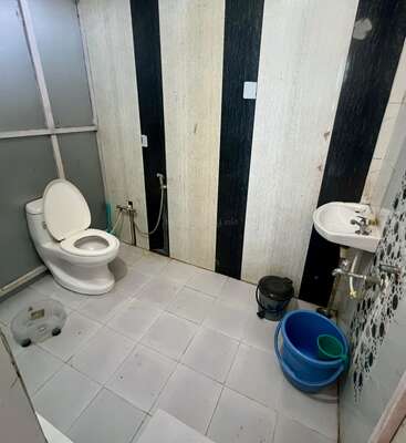 Das ist ein einfaches Badezimmer mit Toilette, Waschbecken, blauem Eimer, Becher, schwarzem Mülleimer, gestreifter Wand und Fliesenboden. Es gibt ein Handbidet.