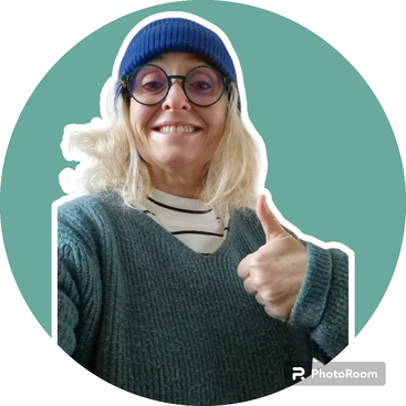 A smiling person with blonde hair wears glasses, a blue beanie, striped shirt, and teal sweater. They give a thumbs up against a green circular background.