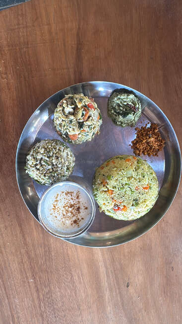 Uma refeição tradicional indiana servida em um prato de aço, com vários tipos de arroz, curry de legumes, chutney, coalhada com especiarias e um chutney em pó seco.