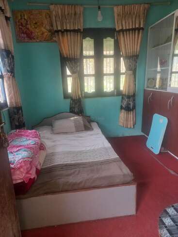 A cozy bedroom with aqua blue walls, brown curtains, a single bed with pink bedding, a glass cabinet, red carpet, and a religious painting on the wall.