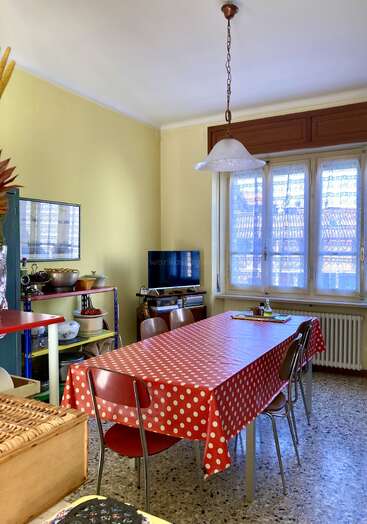 Une salle à manger confortable avec des murs jaunes, un sol en terrazzo et une grande fenêtre. La table est recouverte d'une nappe à pois rouges et entourée de chaises brunes.