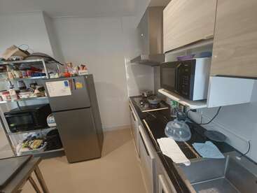 Cette image montre une cuisine compacte avec un réfrigérateur, des étagères métalliques remplies d'aliments, un micro-ondes, une cuisinière, des placards et un évier avec un égouttoir à vaisselle.