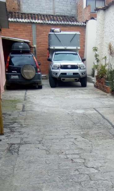 L'image montre une allée avec deux véhicules, un camion argenté et une Honda noire, garés devant un bâtiment en briques dont la porte de garage est ouverte.