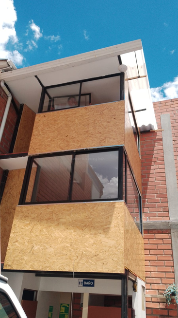 This image shows a three-story building with large glass windows and wooden panels, a bright blue sky, and a bathroom sign visible on the ground floor.