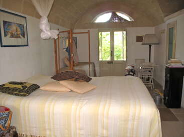This cozy bedroom features a large bed with striped bedding, pillows, a wooden screen, a small writing desk, a lamp, and double doors opening outside.
