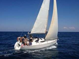 L'image représente un voilier blanc à deux voiles, transportant un groupe de personnes, naviguant sur l'océan par une journée ensoleillée.