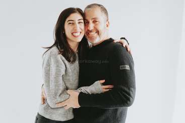 Um homem e uma mulher sorridentes se abraçam alegremente, parados juntos em um fundo branco. Eles parecem felizes, confortáveis e compartilham um momento caloroso e afetuoso juntos.