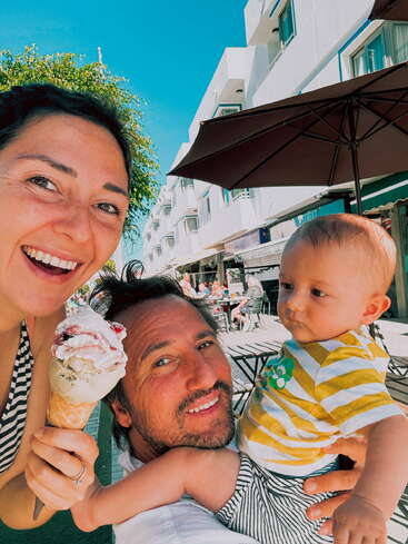 The image shows a family of three enjoying ice cream on a sunny day, with a man holding an infant and a woman holding an ice cream cone.